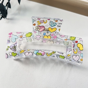 Close-up of transparent heart-pattern hair claw clip with colorful polka dots and text