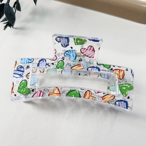 Detail showing a large acrylic hair claw clip with colorful heart patterns and metal spring