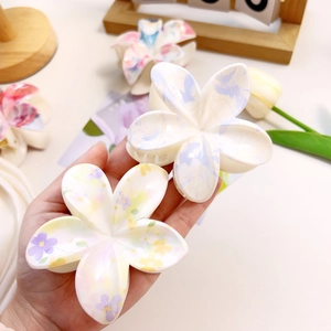Detailed view of floral marble acetate hair claws held by hand to show size and texture