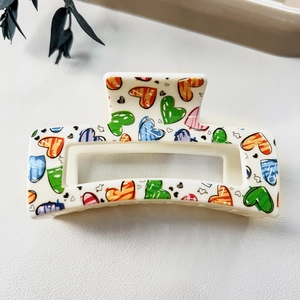 Close-up of a white rectangular hair claw clip with colorful graffiti heart patterns