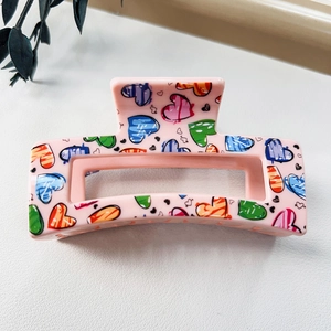 Detail of large pink resin hair claw clip with colorful graffiti heart patterns and textures