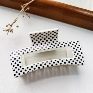 Detailed view of white square hair claw clip with black polka dot pattern and fine teeth