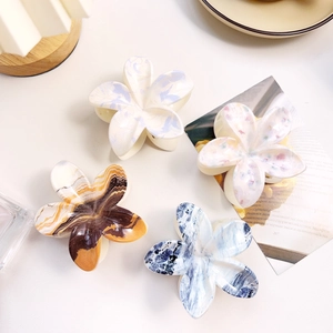 Detail of four marble patterned acetate flower hair claws in blue, amber, and pink colors