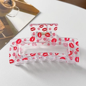 Detail of transparent large hair claw clip with red lip and rose prints on white surface