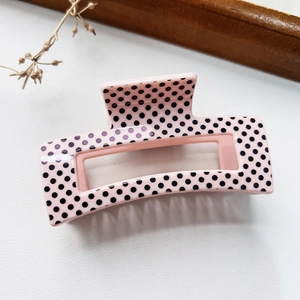 Pink hair claw clip with black polka dots on a textured surface with dried flowers