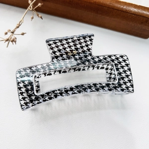 Detail view of houndstooth hair claw clip with golden metal logo on elegant background