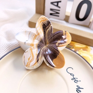 Macro shot of marbled acetate plumeria hair claw clip with golden polished finish