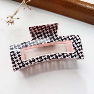 Detail of a pink and black houndstooth pattern hair claw clip on a textured white surface