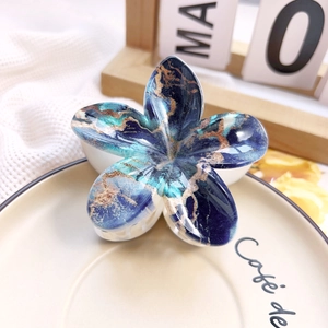 Macro detail of blue marble textured plumeria flower hair claw clip on ceramic dish