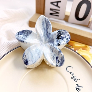 Detailed macro view of frangipani flower hair claw with blue marble texture on ceramic plate