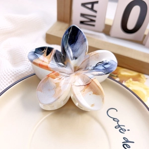 Detailed macro view of plumeria shaped hair claw with artistic ink pattern on ceramic tray