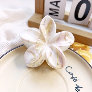 Close-up of frangipani flower hair claw with pink marble pattern on a ceramic dish