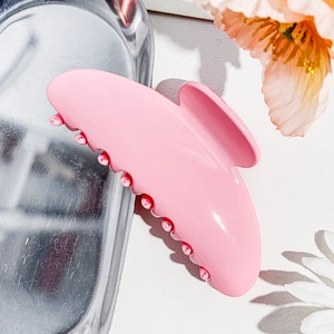 Detailed close-up of glossy pink resin hair claw clip on silver metal tray with floral accents