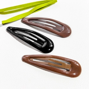 Close-up of black and brown teardrop snap hair clips on textured white leather background