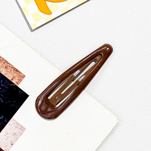 Detailed macro view of dark brown gloss finish metal teardrop hair clip on textured surface