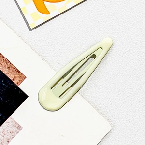 Close-up of a creamy yellow water-drop metal snap hair clip on a textured background