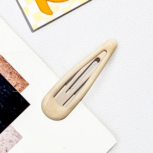 Detail of a beige teardrop snap hair clip with a glossy finish on white leather