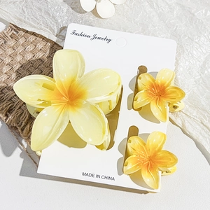 Close-up of three yellow plumeria hair claws in various sizes on a white product card