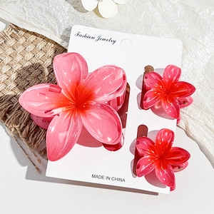 Detailed set of three pink gradient plumeria hair claws on a rustic fabric background