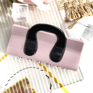 Detail view of pink and black hair claw clip with sturdy teeth on a textured background