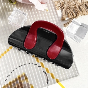 Detail view of a black and wine red contrast hair claw clip on a stylish display board