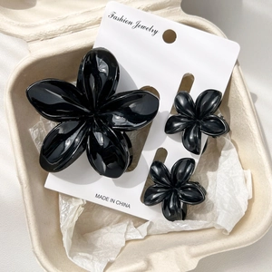 Detailed macro view of three glossy black flower hair clips in various sizes for styling