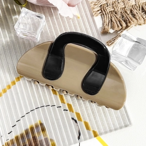Detail of khaki and black contrast hair claw clip on a stylish textured glass surface