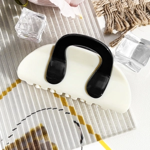 Detail view of cream-colored shark hair clip with black U-shaped contrast accents