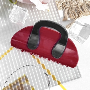 Detail view of burgundy and black color-block hair claw clip on a decorative background
