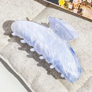 Close-up of light blue marble textured hair claw clip on soft cream fabric background
