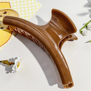 Glossy caramel large hair claw clip for thick hair shown on a white leather background
