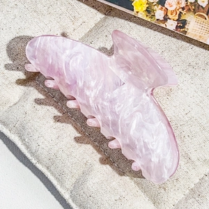 Detailed macro view of cherry pink marble textured acetate hair claw clip on beige fabric