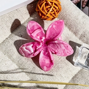 Dettaglio macro di un fermaglio per capelli a fiore in acetato rosa marmo su lino beige