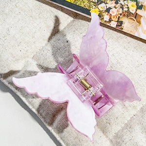 Detail view of pink marble butterfly hair claw clip with golden spring on linen fabric