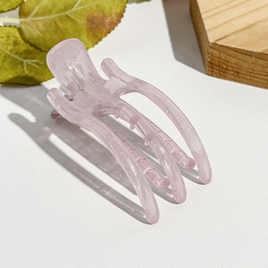 Makroansicht der rosa-transparenten Haarklammer auf Naturholz mit grünen Blättern