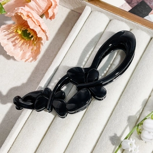 Macro shot of glossy black butterfly hair clip with polished finish on beige velvet