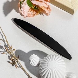 Close-up of a matte black metal barrette with a sleek minimalist curved design and texture