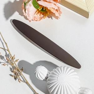 Detail shot of a dark brown oval spring hair clip on a textured white surface background