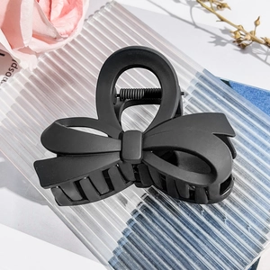 Detail showing the matte black bow hair claw clip on a textured display board