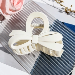 Close-up of cream-colored bow hair claw clip with matte finish on elegant glass tray