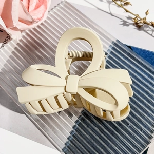 Macro detail of creamy bow hair claw clip showing textured matte finish and strong spring