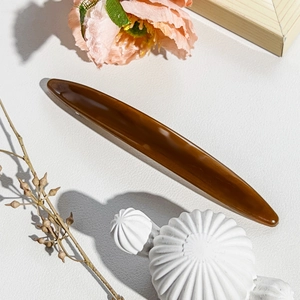 Close-up of a long amber tortoiseshell hair clip on a soft floral decorative background