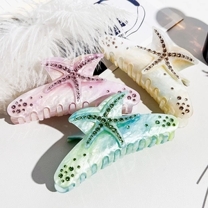 Detail of star-shaped hair claws with rhinestone accents on marble texture surface