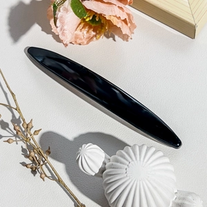 Polished black obsidian gua sha massage tool on luxury leather background with floral decor
