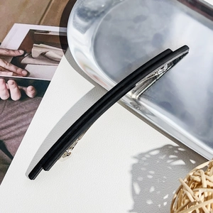 Detail of matte black minimalist spring hair clip on a metallic tray with natural lighting