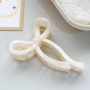 Detail of a creamy white bow hair claw clip with marble texture and gold spring