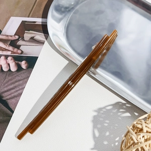 Close-up of a glossy translucent brown acrylic hair clip on a minimalist white leather surface