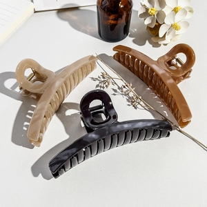 Trois grandes pinces à cheveux en noir, beige et marron sur un fond de style minimaliste