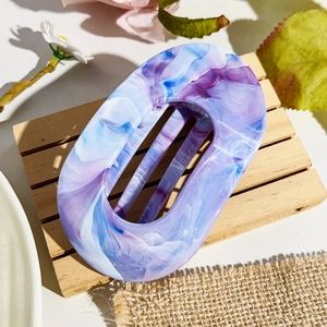 Detail view of oval marble-patterned hair claw clip on a rustic wooden tray decoration