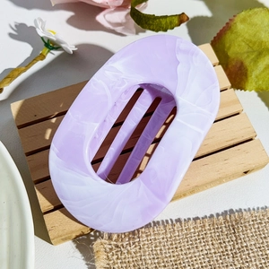 Detail view of purple marble acetate hair claw clip on wooden tray with floral decor